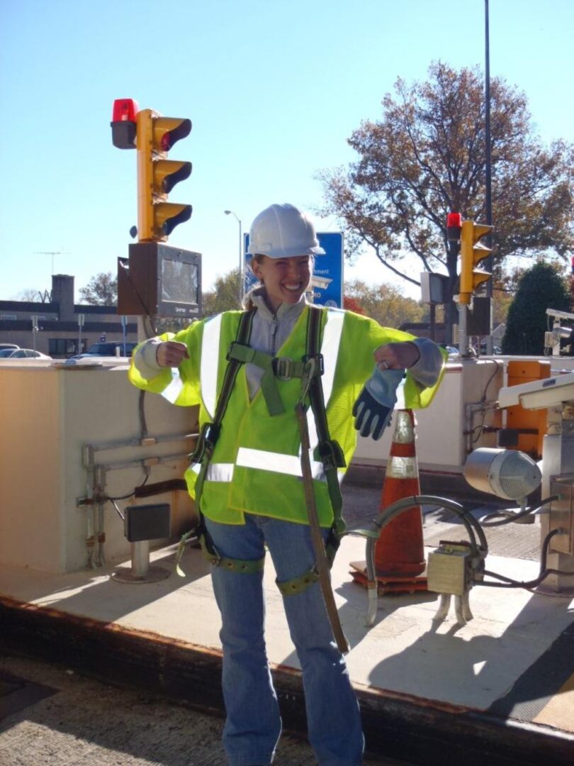 A woman in yellow vest and hard hat standing on street.