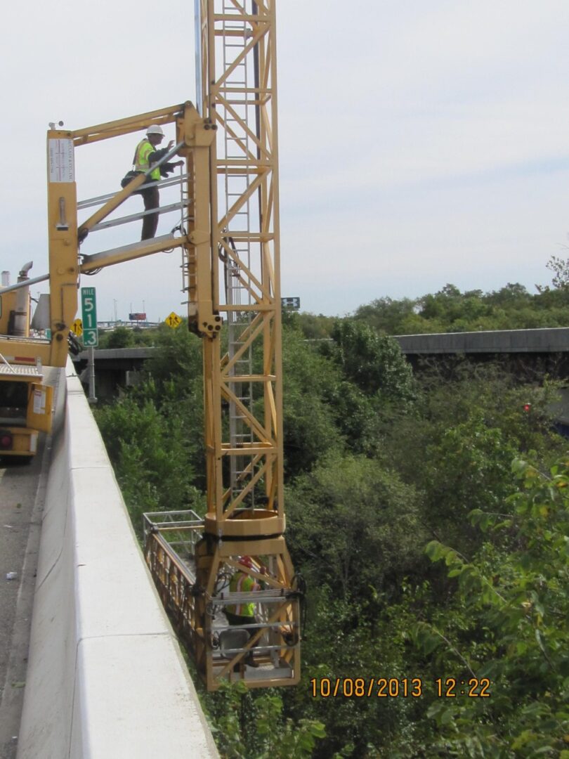 A construction worker is working on the side of a bridge.